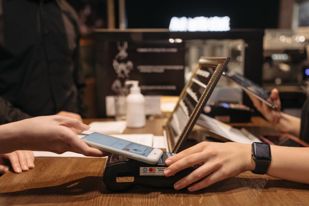 a-person-tapping-the-phone-on-a-payment-terminal-6612717 Hands using mobile for contactless payment at café terminal.