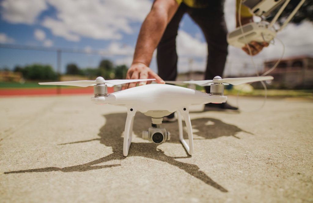 man-preparing-drone-3018067 A white drone is prepared for flight on a sunny day with blue skies.